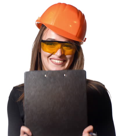 cheerful girl engineer in black jumper and a bright helmet emotionally talks about business, with gesturing and holding a folder-holder and a pen in her hands on a white background.