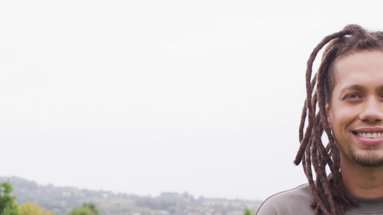 Uomo afroamericano con felpa girocollo grigia che sorride, ridendo mentre la telecamera si sposta a destra sulle colline, con spazio per il testo