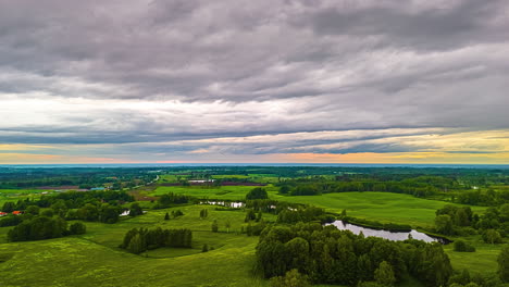 a dramatic aerial timelapse shows fast-moving grey clouds at sunset sweeping over a beautiful, rolling landscape of green hills, forests, and lakes in the latvian countryside