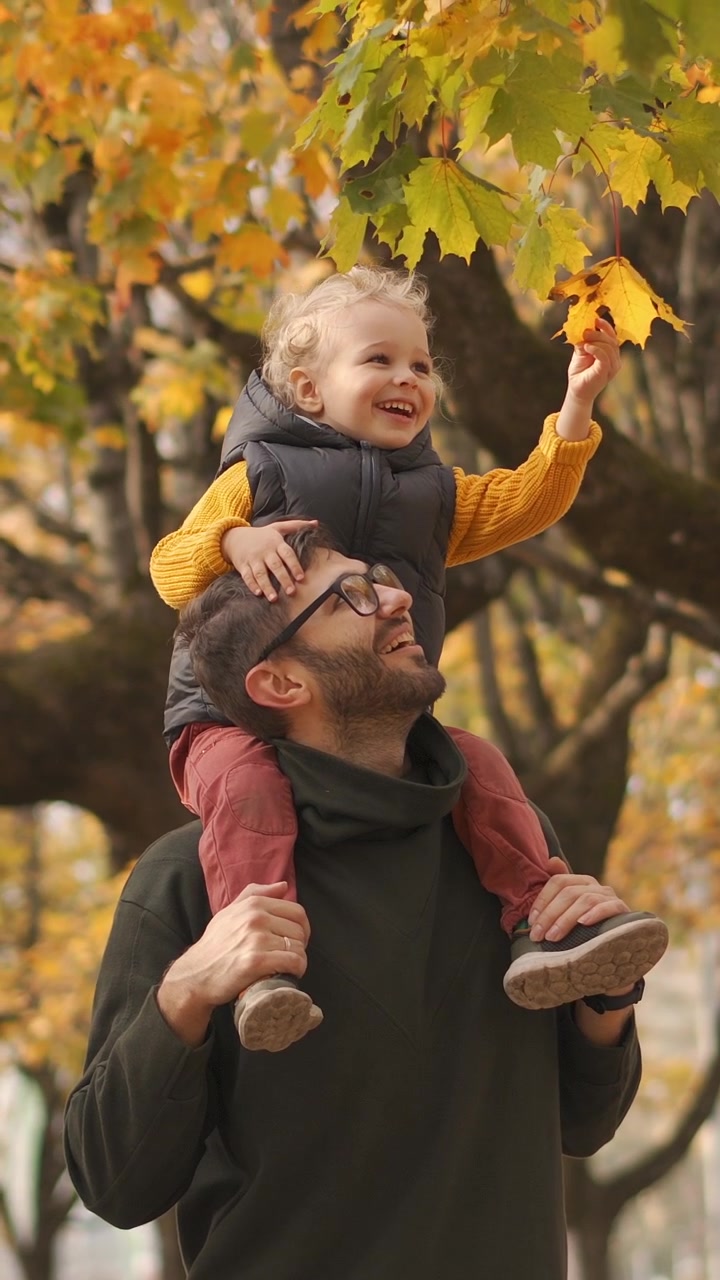 Padre che porta il bambino piccolo sulle spalle in un parco autunnale