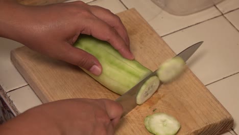 hands slicing a cucumber on a cutting board