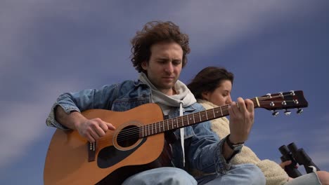 a young boy plays the guitar and a young girl looks around with a pair of binoculars on the roof of a caravan.