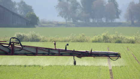 boom arm of sprayer tractor spraying insecticide over crops on farm land