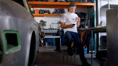 Male-mechanic-having-coffee-while-using-mobile-phone-4k