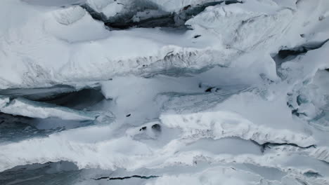 aerial close up top down view of the cracks of the face of a large glacier on a sunny day in winter in the alps