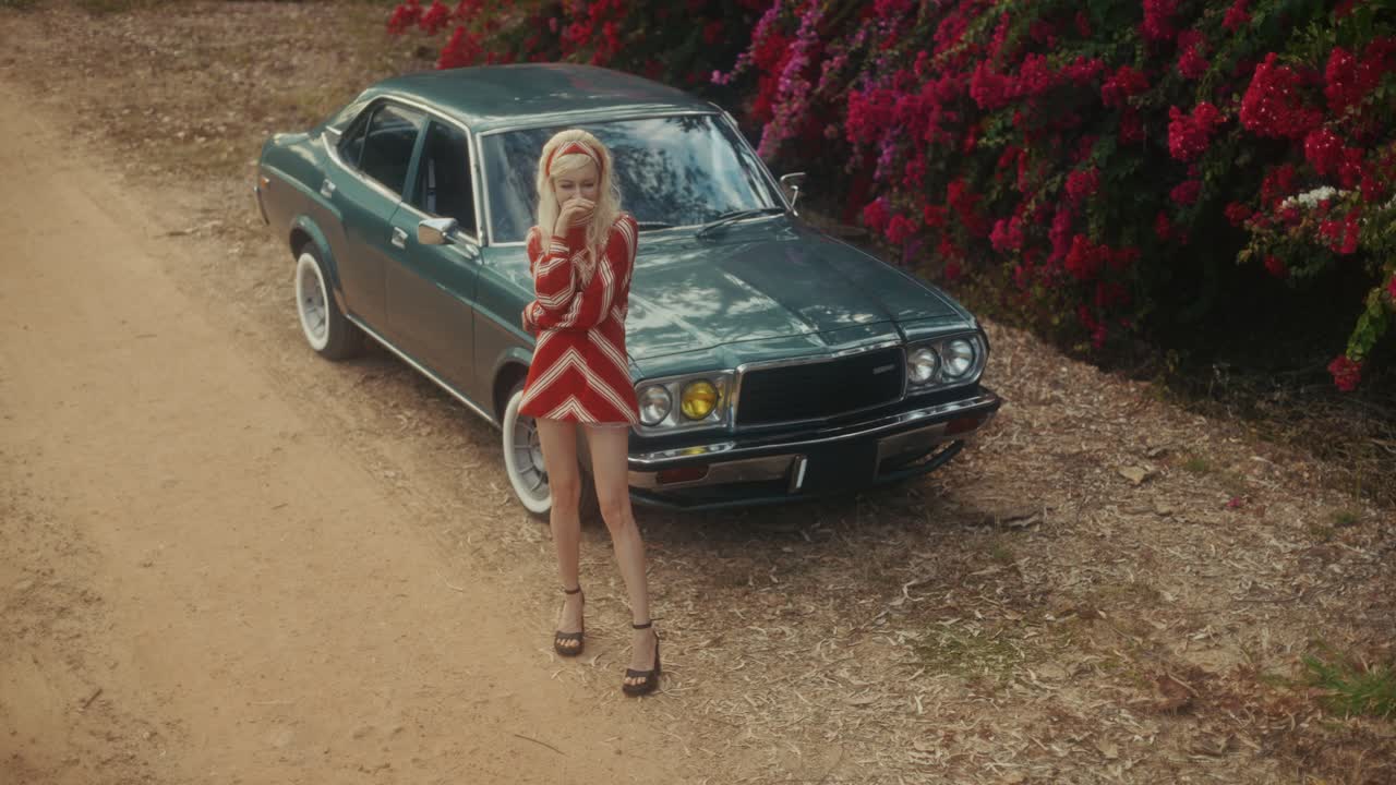 Mujer elegante posando con un coche clásico en un camino de tierra