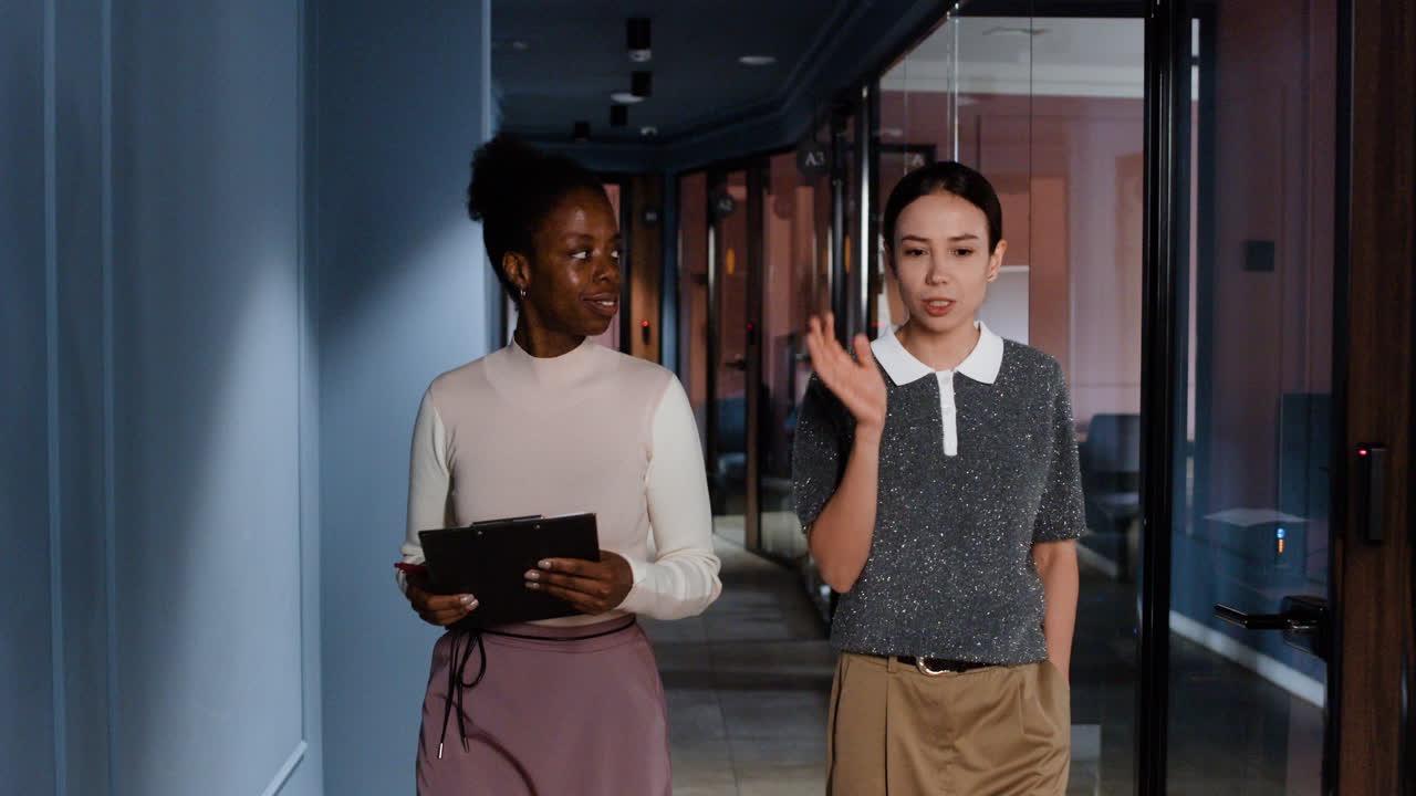 Two Businesswomen Discussing and Walking in an Office Hallway