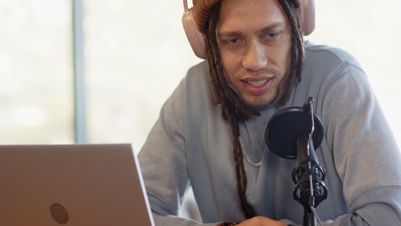 African American male podcaster adjusting headphones, speaking into mic in studio for podcast
