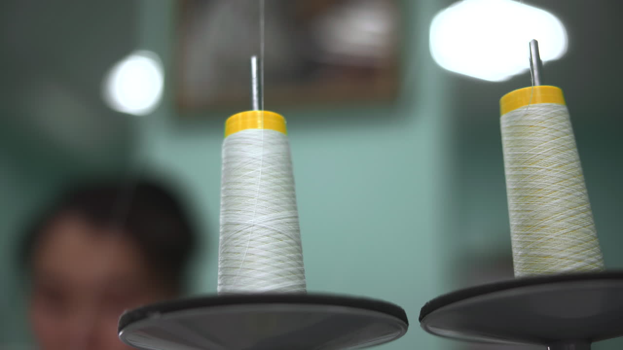 Macro Thread Spool With Blurred Operator Background. Two Tall Spools And Bobbin Holders In Soft Light. Media