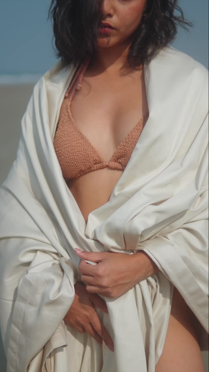 Vertical Close-up of woman in bikini wrapped in white fabric standing on sandy beach