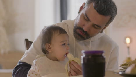 Apuesto-Padre-Barbudo-Alimentando-A-Su-Hija-Con-Plátano-1