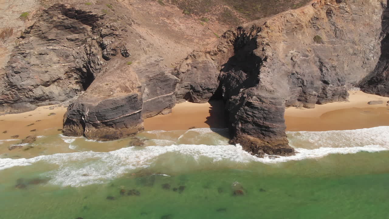 Scenic View Of Bright Blue Sea Waves Splashing On The Rocky Shore In Slow Motion At The Beach In Algarve, Portugal - aerial drone, pullback shot