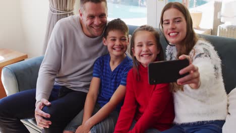 familia caucásica sonriendo mientras tiene una videollamada en el teléfono inteligente sentado en el sofá en casa