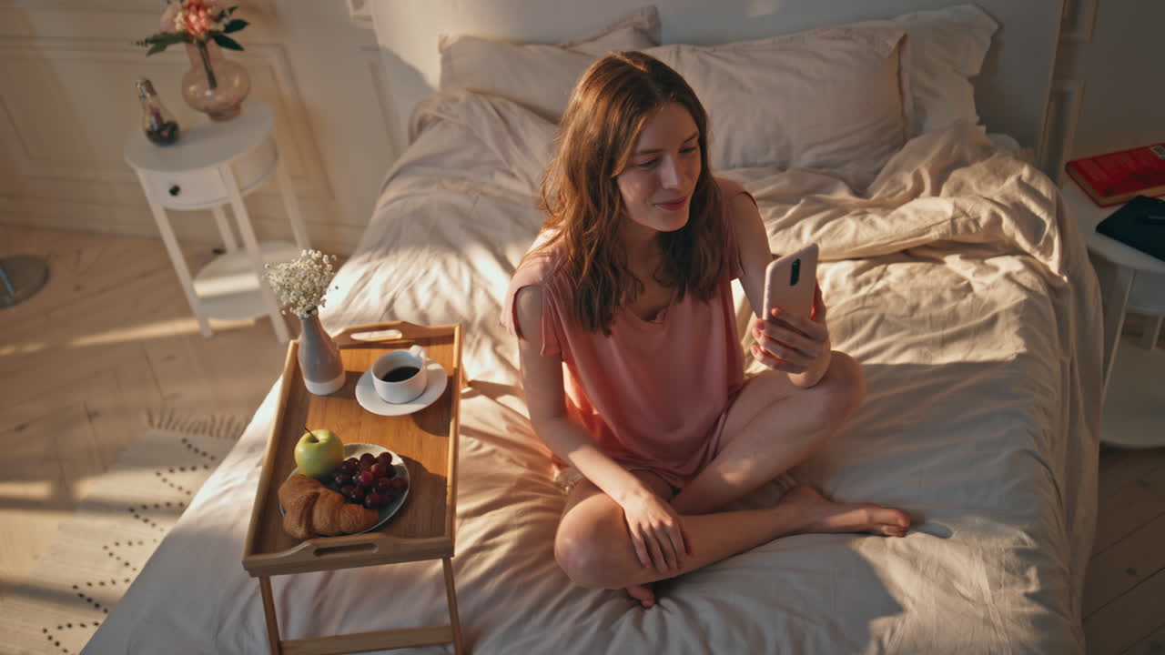 спокойная девушка звонит онлайн с помощью смартфона в постели. улыбающийся подросток разговаривает видео