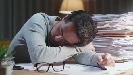 close up of tired asian man sleeping due to working hard with documents at home