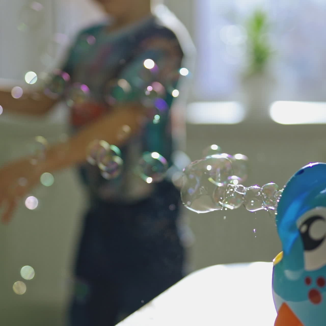 Boy's hand is switching on bubble device and playing happily at home. Bubble blower in the form of blue fish creating round bubbles into the room inside. Soap bubbles and small boy.