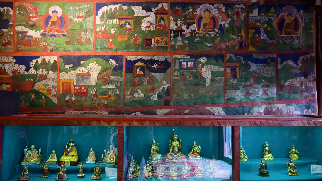Ancient Buddhist art inside Erdene Zuu Monastery, Mongolia: vibrant historic wall murals and a collection of small gilded deities in a glass display showcase traditional religious craftsmanship