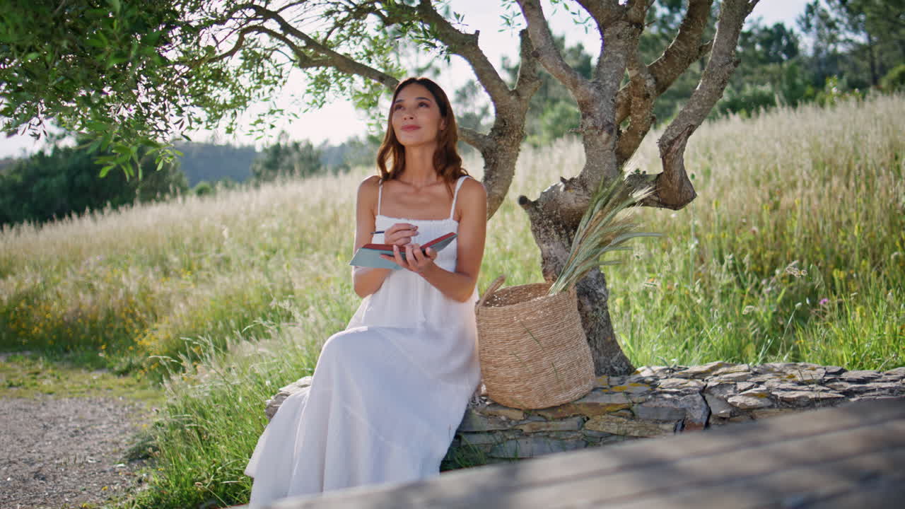 Girl writer noting information copybook sitting wooden log. Woman putting marks