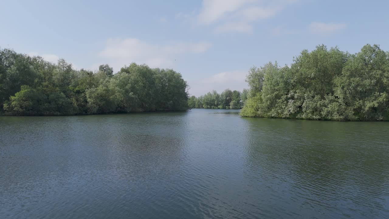 Droneoptagelser, der flyver lavt over en rolig sø, mens kajakroere sætter i vandet, omgivet af frodigt grønt. Perfekt til vandsport, udendørs eventyr og naturscener