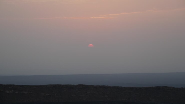 Landscape shot of a sun covered with clouds, rising from the sky