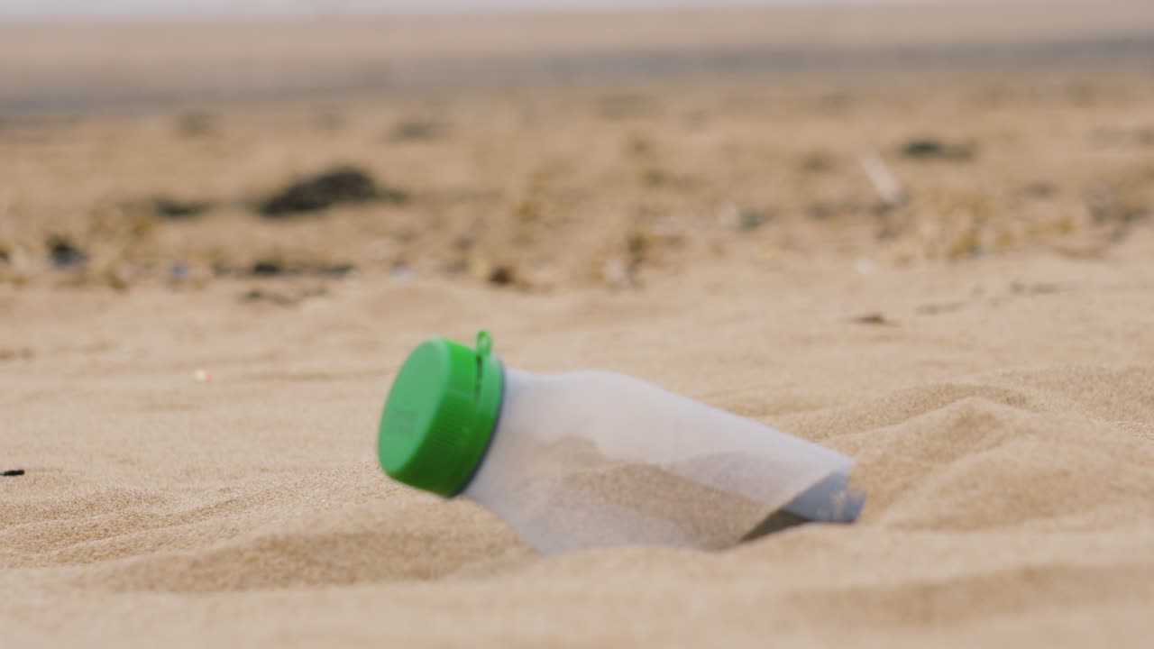Focus from Sandy Beach to Plastic Bottle Stuck in Soft Sand After Being Littered Causing Pollution and Potential Harm to Marine Sea Environment