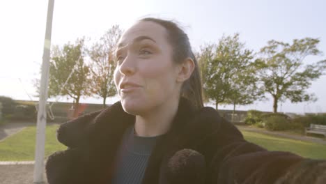 mujer sonriendo y hablando con la cámara en una videollamada en un parque con un hermoso destello de lente