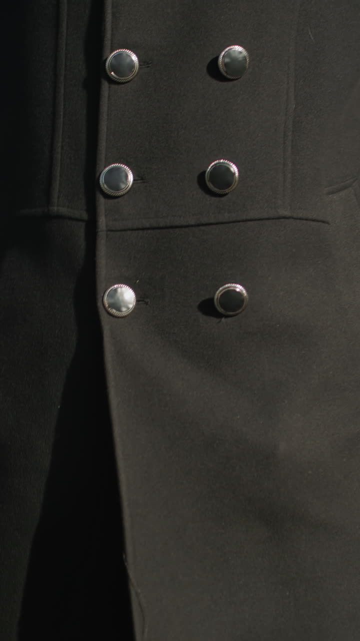 primer plano de un político caminando con confianza al aire libre sosteniendo un maletín, usando un elegante abrigo negro con botones metálicos, rodeado de arquitectura urbana moderna, árboles verdes y un cielo azul claro