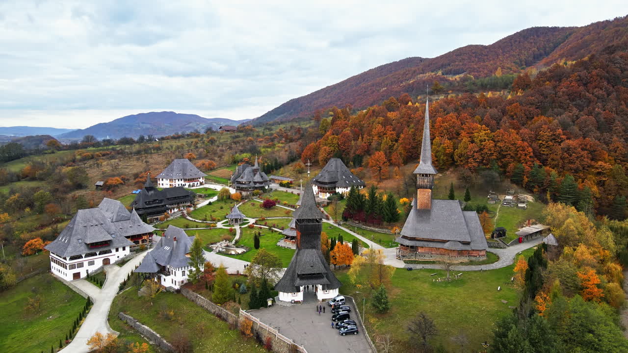 Aerial drone view of the Barsana Monastery, Romania. Main church and other buildings, visitors, hills covered with yellowing forest around