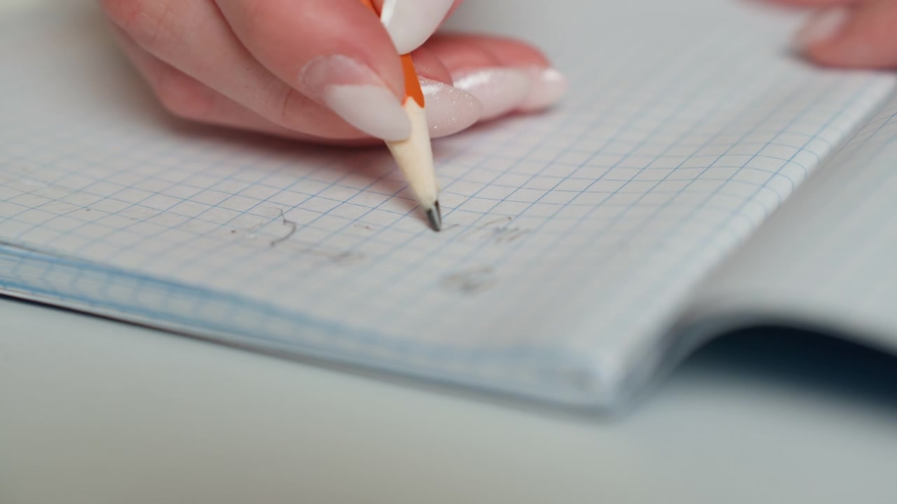 Primo piano di una mano con manicure che corregge i compiti in un quaderno a quadretti, segni precisi a matita, segni di correzione ordinati, atmosfera di feedback positivo, umore da revisione del coach, scrivania luminosa di giorno, progresso e miglioramento