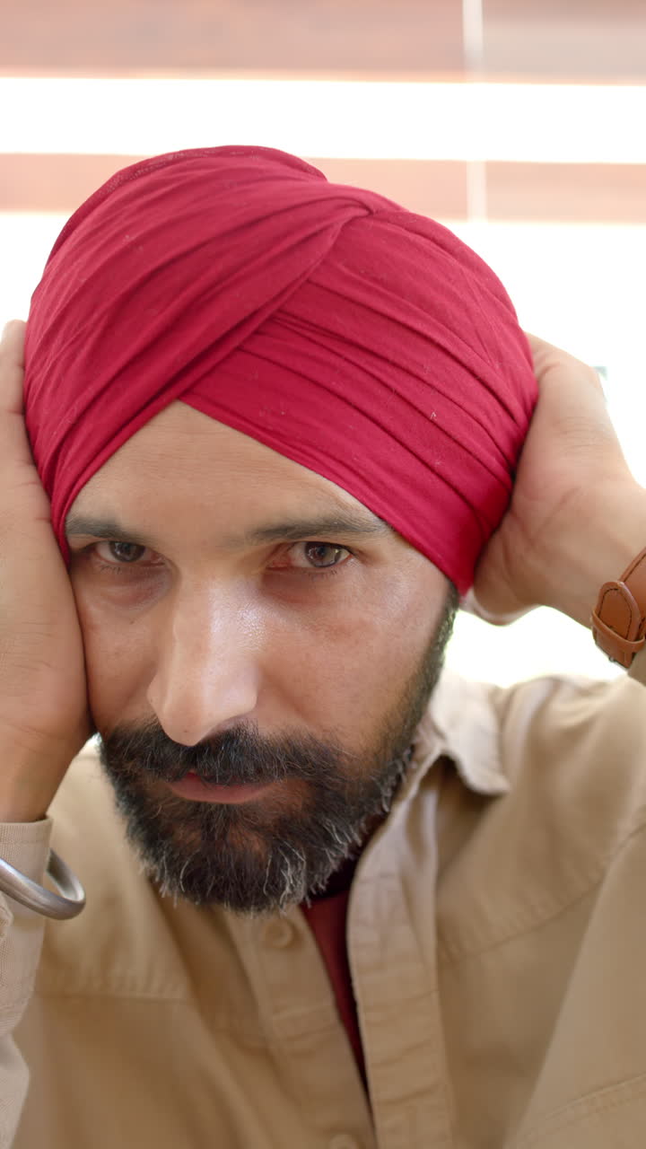 Vertical video: Adjusting red turban, man looking at camera with serious expression