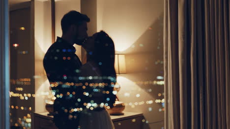 romantic couple embracing by window with city lights at night
