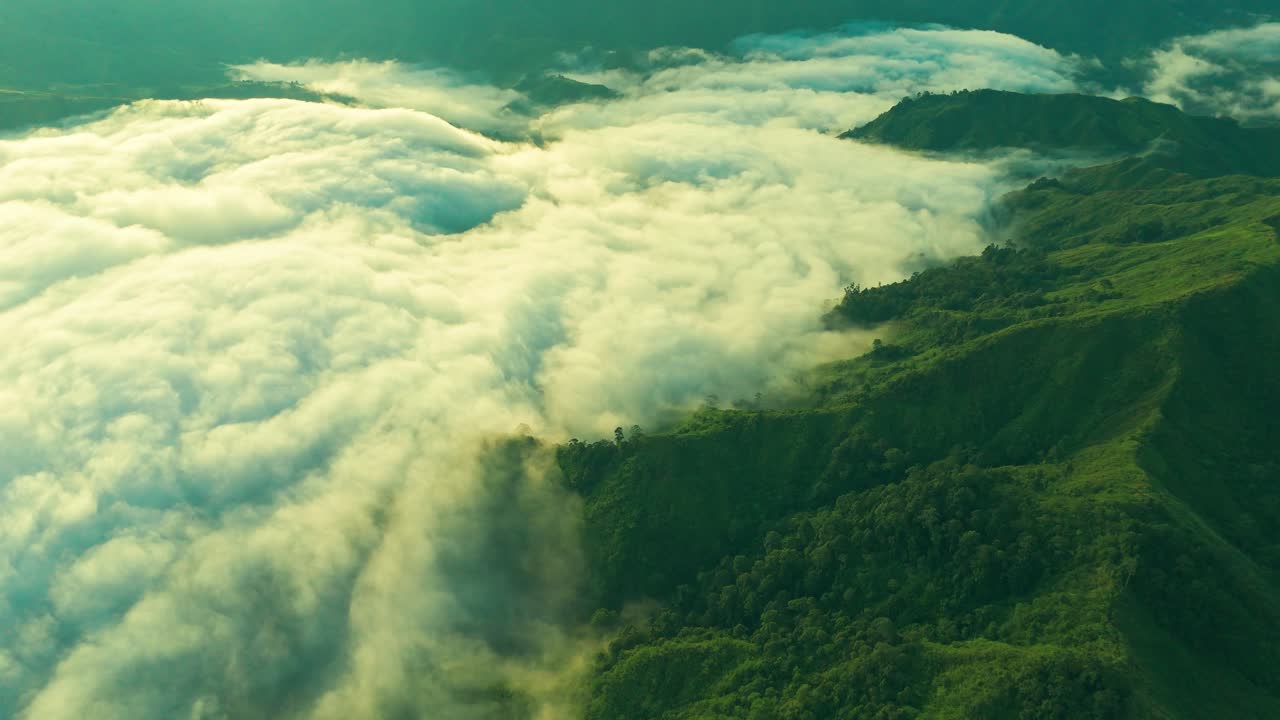 Aerial drone view of golden sunlight reflecting on thick rolling clouds above lush green mountain ridges, perfect for travel, eco projects, documentaries, cinematic storytelling