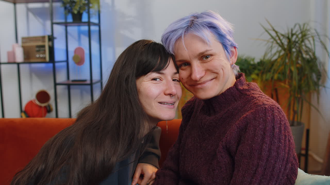 Loving female lesbian women family couple hugging relaxing together looking at camera at home