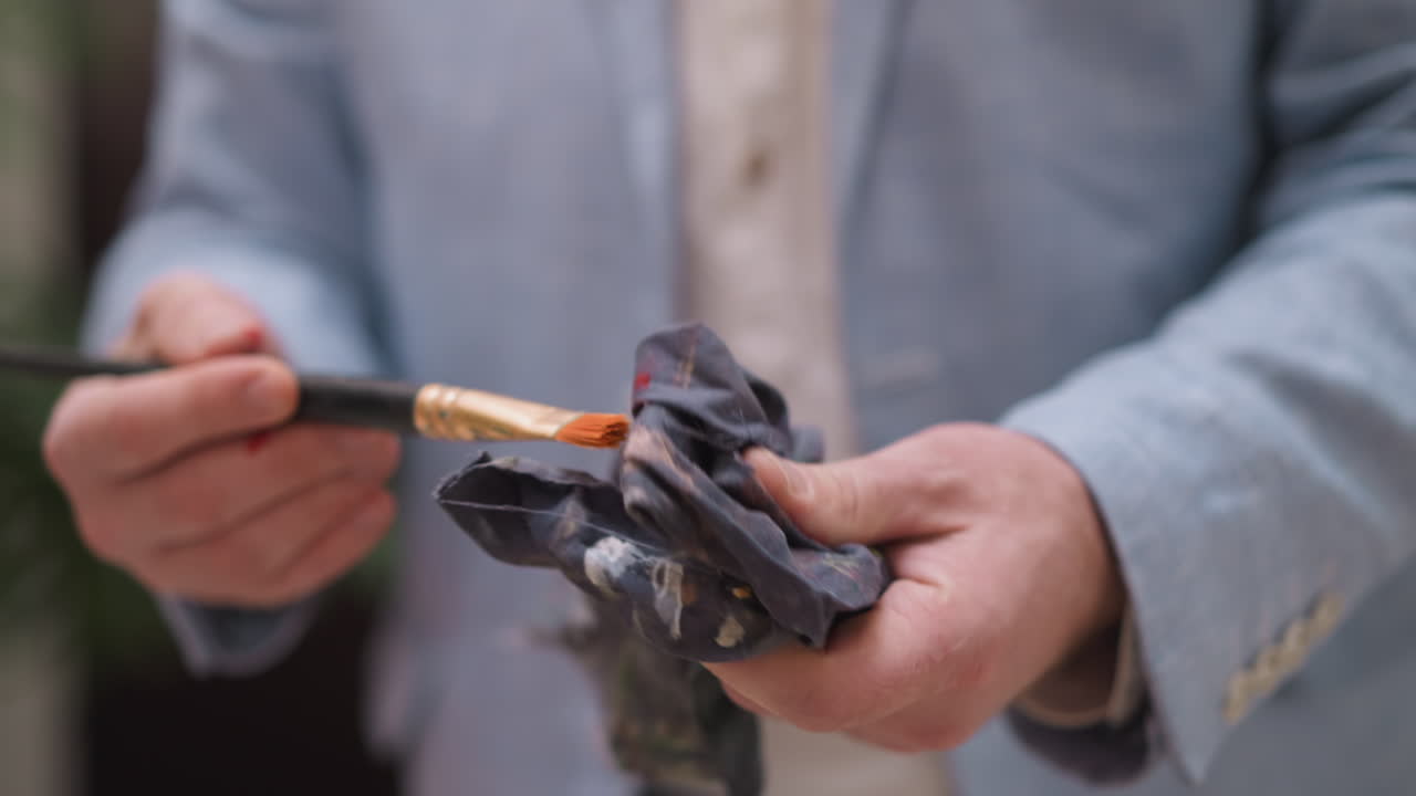 мужчина-художник вытирает щетку тканью. профессиональный художник-мужчина в куртке обеспечивает точность и чистоту в процессе создания искусства вблизи