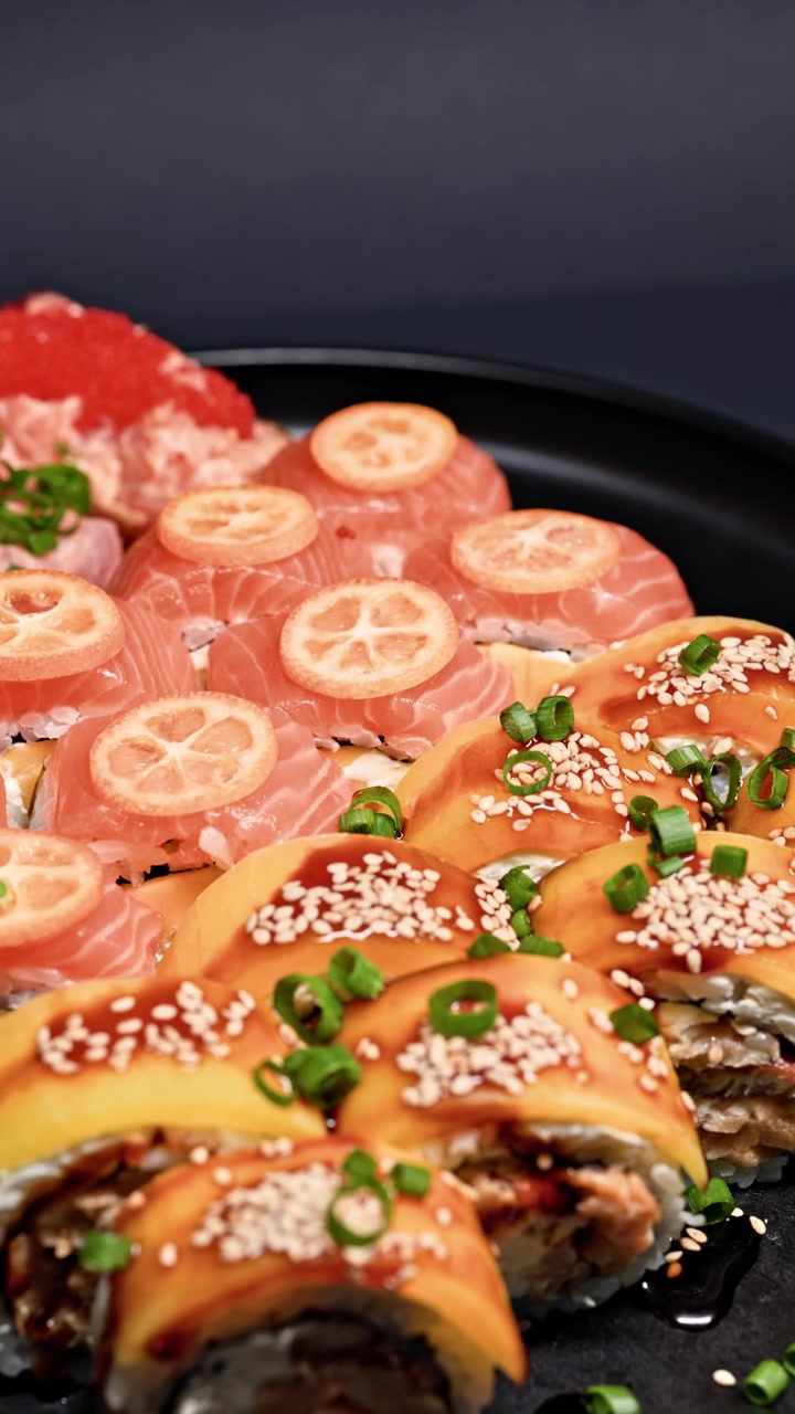 黒い皿に盛り付けられた、サーモン、レモン、トッピングが乗った色鮮やかな寿司の盛り合わせ。