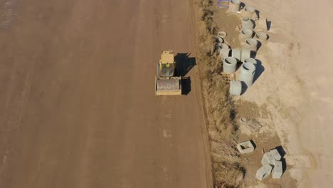 aerial following shot of a bulldozer roller compacting dirt in a field next to drain pipes