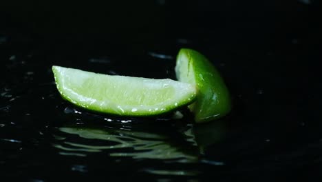 Frisches-Stück-Grüner-Limette-In-Zeitlupe,-Das-Auf-Die-Plätschernde-Wasseroberfläche-Fällt,-Isoliert-Auf-Schwarz,-Kochkonzept