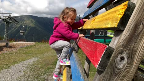 cute young little girl climbing colored ladder in slow motion with mountains in the background