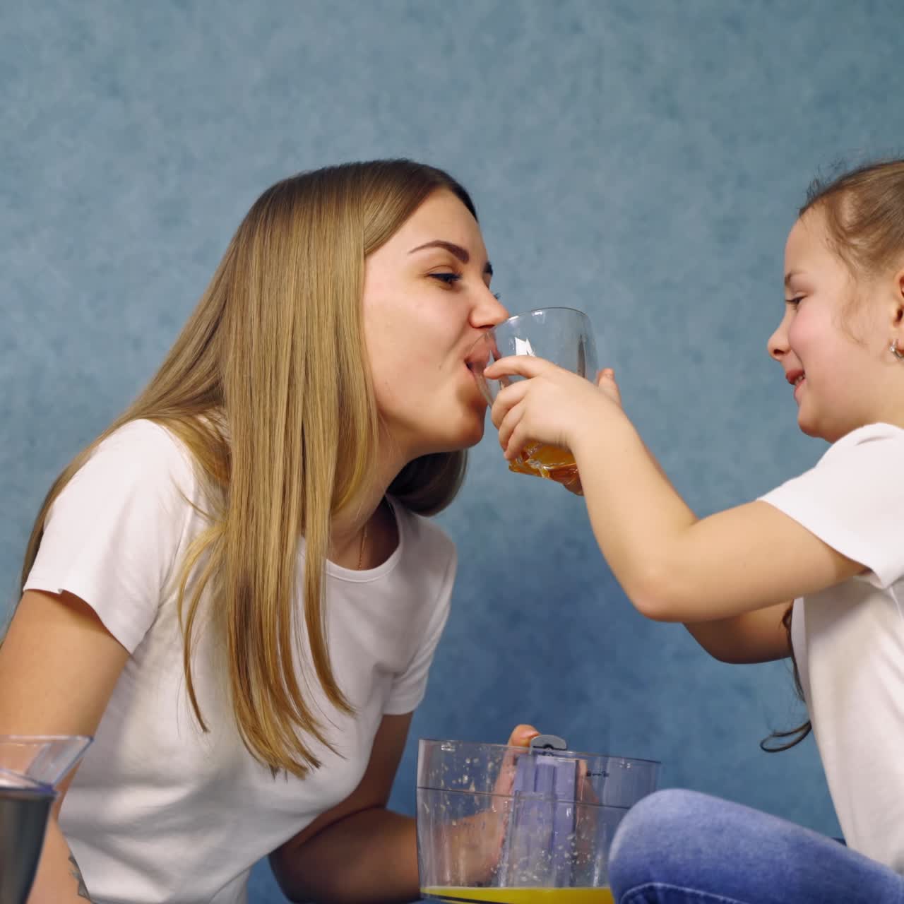 Little girl giving fresh juice to her mother. Happy mother drinking freshly squeezed orange juice at home. Healthy drink.