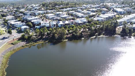 Drone-flying-over-a-manmade-lake-towards-an-upmarket-suburb-with-large-family-homes-in-Australia