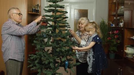 Kleines-Mädchen-Mit-Großmutter-Und-Großvater,-Die-Einen-Künstlichen-Weihnachtsbaum-Mit-Spielzeug-Dekorieren