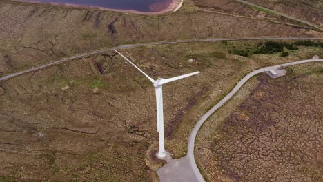 disparo de avión no tripulado centrado en una turbina eólica cerca de un lago y una carretera de una sola vía