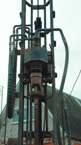 machine details rotate and shake as the equipment boring the well. low angle view. rural house at backdrop. vertical video.