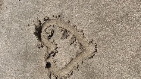 vertical tracking shot of a heart drawn in the wet sand of the beach