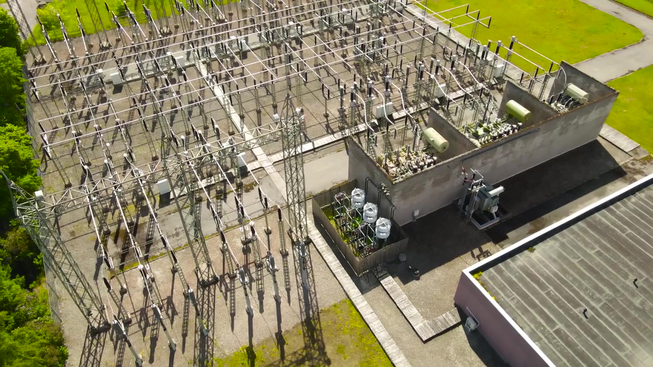 Vysokonapěťová elektrárna generující a distribuující elektřinu se složitou sítí kabelů, věží, izolátorů a transformátorů pro dodávku energie za slunečného letního dne