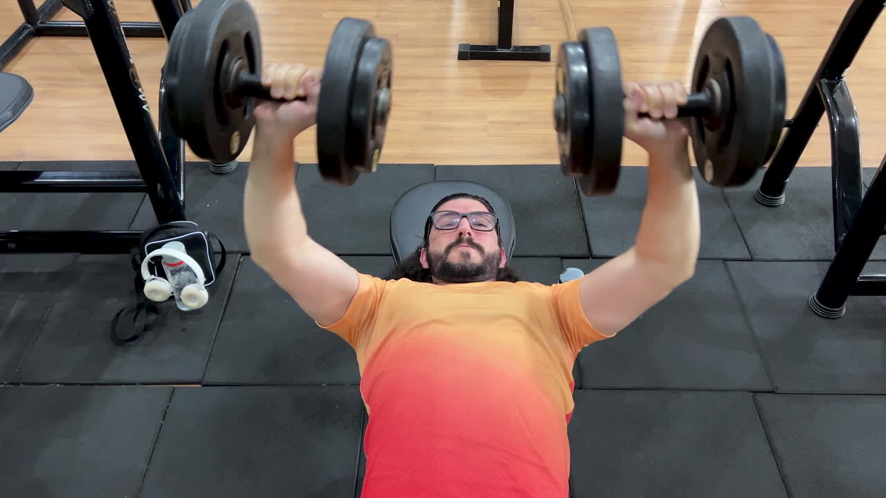 Homem latino com barba e cabelo comprido realizando movimento de supino com halter