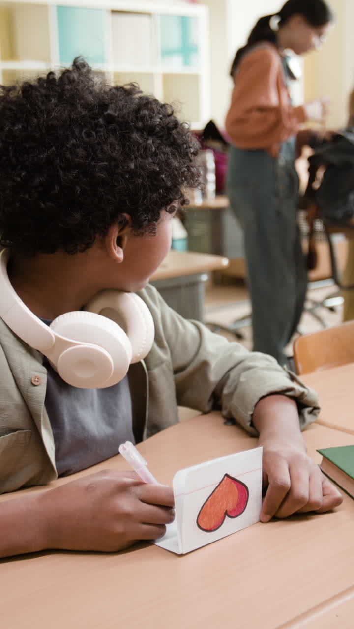 A young student draws a heart on a paper in a classroom