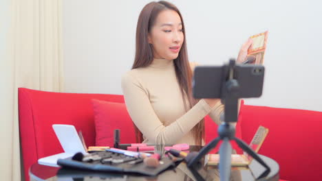 Asian-Woman-Present-Beauty-Cosmetic-Product-and-Broadcast-Live-Video-to-Social-Network-by-Internet-Via-Mobile-Phone-at-Home,-beauty-blogger-concept