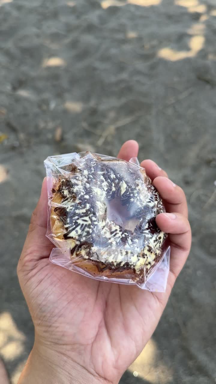 Mano che tiene e ruota una ciambella con granella di cioccolato.