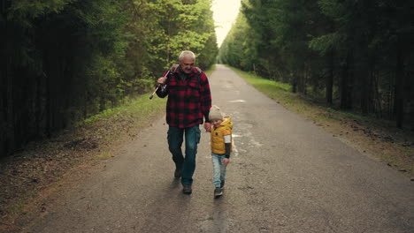 Un-Chico-Divertido-Y-Su-Abuelo-Caminan-Hacia-La-Pesca-Paseando-Por-La-Carretera-A-Través-Del-Bosque-De-Coníferas.